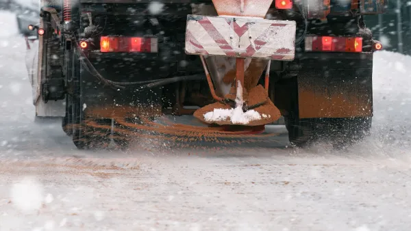 Close-up on back of yellow truck putting down road salt on icy road.