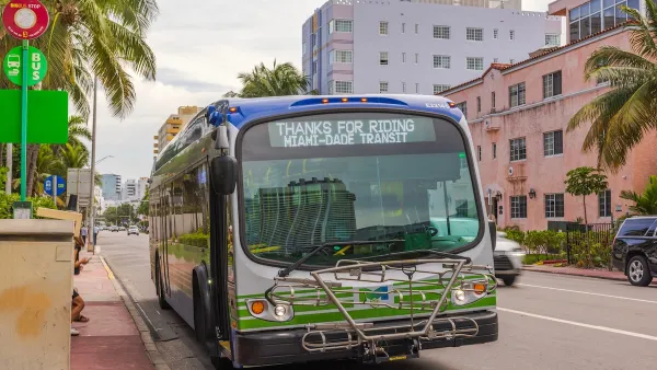A Miami-Dade green bus, surrounded by brick buildings.