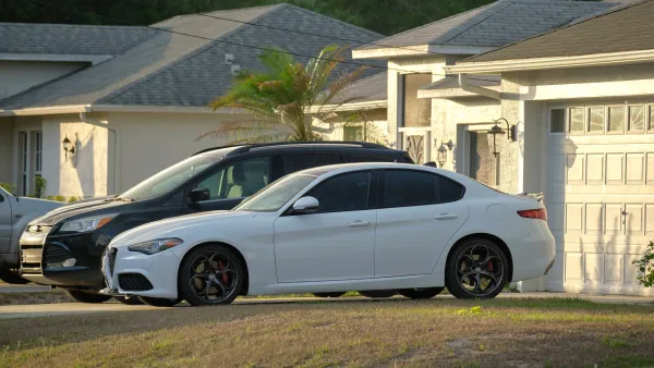 Black SUV and white sedan parked in driveway in front of house.