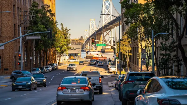 Cars on a small street with view of bridge over bay in San Francisco, California.