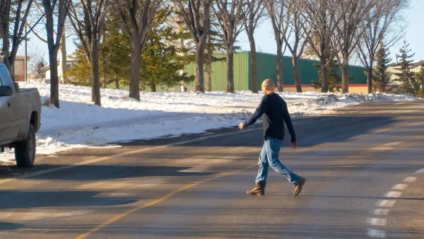 Man in jeans and black shirt crossing street mid-block in winter.