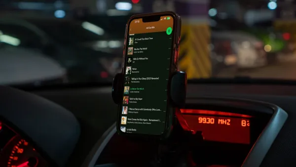 Close-up on phone in car dashboard holder with Spotify playlist pulled up.