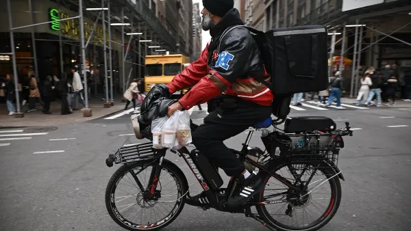 Man with beard and black beanie riding e-bike with delivery cargo.