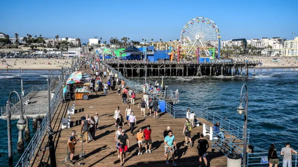 People walking on Santa Monica Pier boardwalk with Ferris wheel visible close to shore on sunny day.