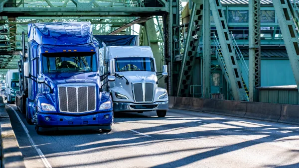 Two large trucks cross the I-5. One is blue, to the right is a white truck.