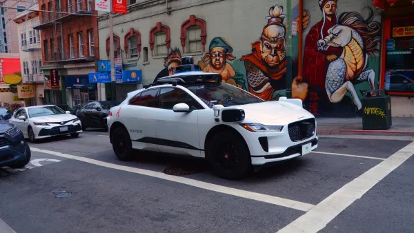 White Waymo Jaguar car on street with colorful mural in background in San Francisco, California.