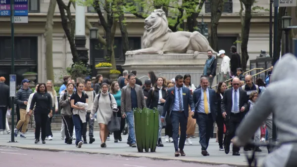 Busy sidewalk in New York City in front of NY Public Library with large stone lion statue.