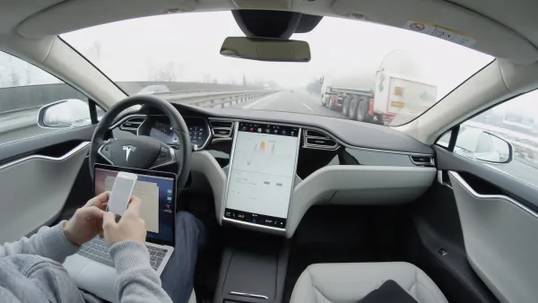 Interior view of man sitting in driver's seat of Tesla car holding laptop and mobile phone in lap.