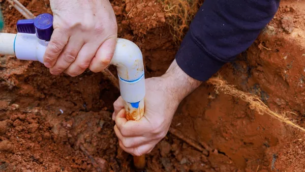 Two hands install a water pipe in red dirt.