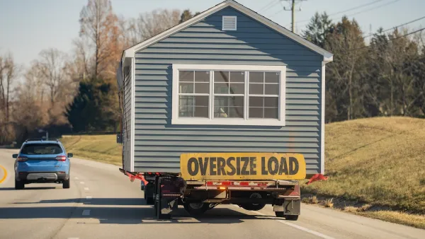 A manufactured house on the back of a truck driving down a road.