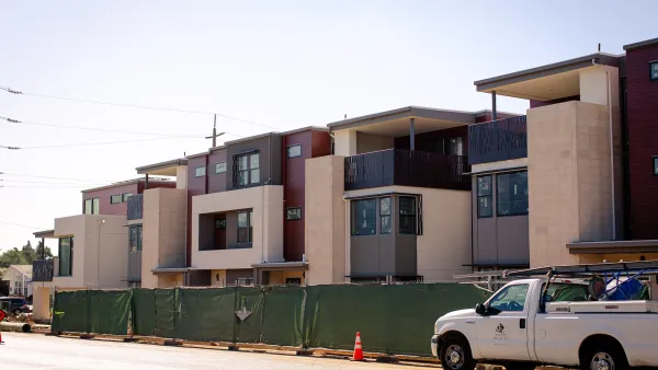 Two-story apartment or condo building under construction behind green construction fence in Cupertino, California.