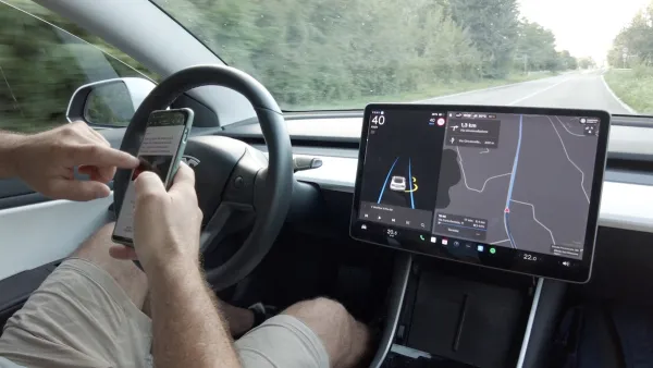 Person texting while at the wheel of a Tesla vehicle implying self-driving features.