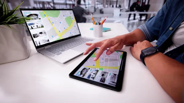 Person with laptop and tablet on desk looking at real estate listings.