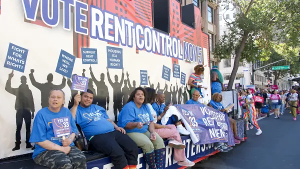 Float supporting rent control with "Vote rent control now" banner behind several sitting people drives through Oakland Pride parade in 2024.