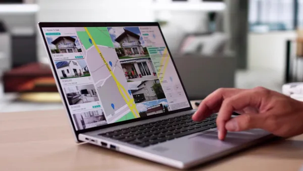 Close-up of laptop with real estate listings open and hand operating mouse trackpad.