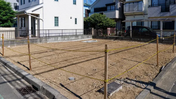 Vacant dirt lot surrounded by yellow and black rope among two-story houses.