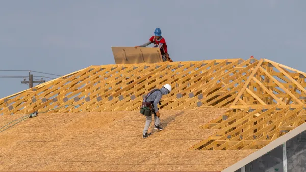 Two construction workers on roof of wood-framed house.