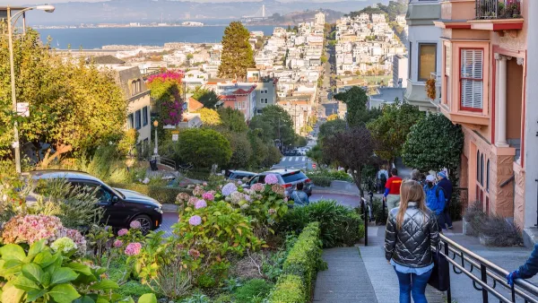 View from top of hill in San Francisco with people walking down sidewalk next to historic Victorian homes.