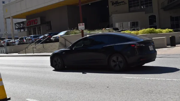 Black Tesla car on street in Houston, Texas next to building with red sign for AMC movie theater.