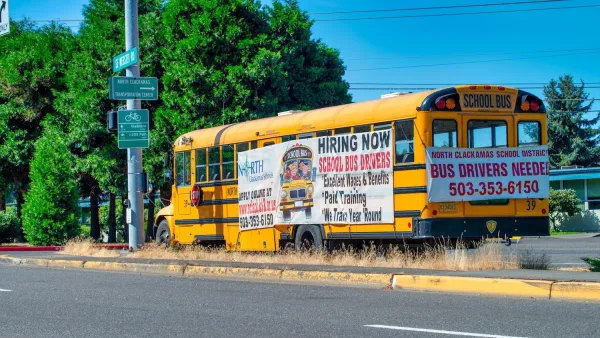 Yellow school bus parked on roadside with signs advertising bus driver jobs.