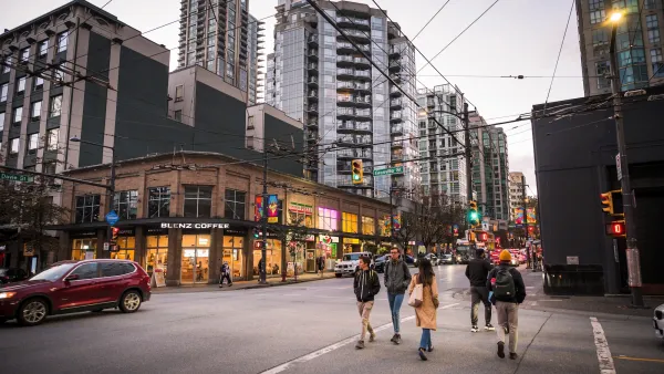 People in a crosswalk in downtown Vancouver, BC with tall glass apartment towers in background and streetcar cables criss-crossing above the street.