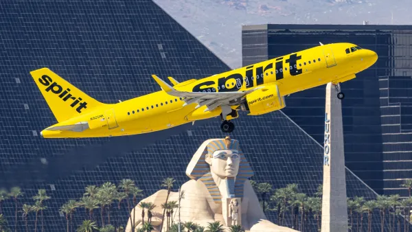 Yellow Spirit Airlines plane taking off in Las Vegas with replica pyramid and Sphynx in background.