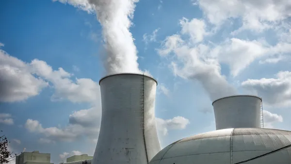 Two large cooling towers with white steam rising out at nuclear power plant.