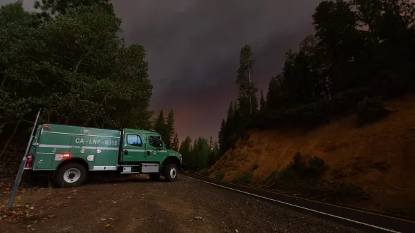 Green wildland firefighting truck parked on road with wildfire sky in the distance.