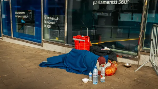 Unhoused person sleeping under a blue blanket on sidewalk next to European Union