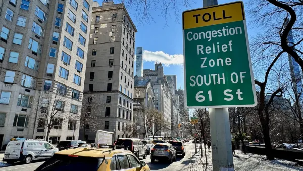 Green and yellow congestion peicing zone sign on post in NYC next to street with moderate traffic.