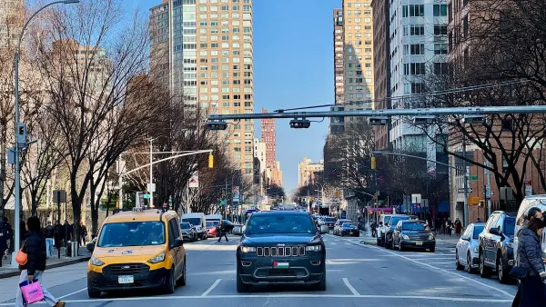New York City crosswalk with a few pedestrians and yellow cab and black SUV stopped at light.