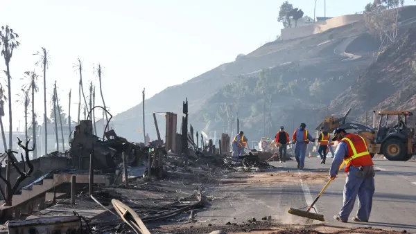 People in orange safety vests sweeping and cleaning debris in Eaton Fire burn area in Malibu.