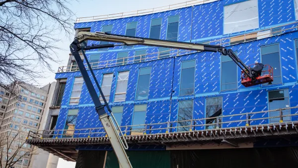 Construction crane in front of apartment building under construction with blue unfinished facade in Philadelphia.
