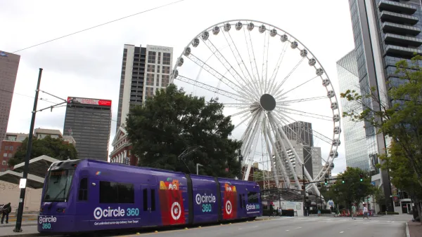 View of giant Ferris Wheel in downtown Atlanta, Georgia in Centennial Olympic Park. Purple public tram (light rail vehicle, popular streetcar) stops in front.