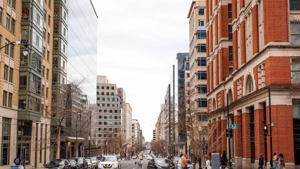Street scene in Washington DC with mixed modern and brick buildings and pedestrians crossing a crosswalk.