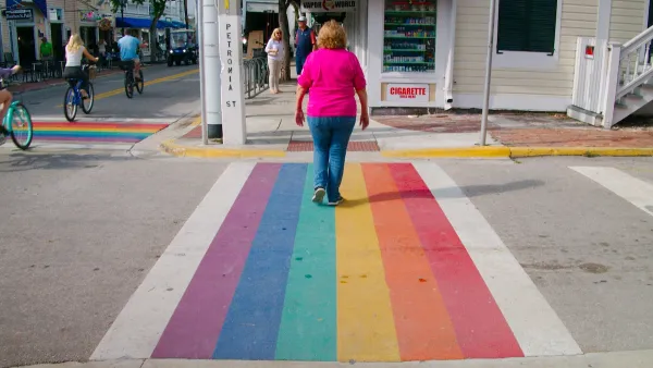 Older white woman in pink shirt and blue jeans walking across Rainbow crosswalk in Key West, Florida.