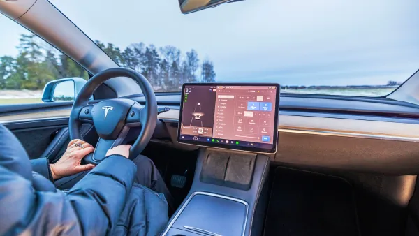 Interior of Tesla car with person's hands on steering wheel and large screen in middle.