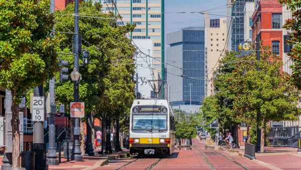 A white and yellow Dallas DART light rail train on track on street paved with red bricks in downtown Dallas, Texas.