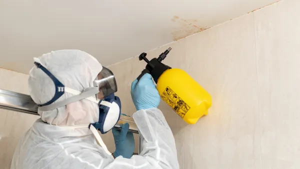 A professional in hazmat gear cleans mold off a white wall and ceiling.