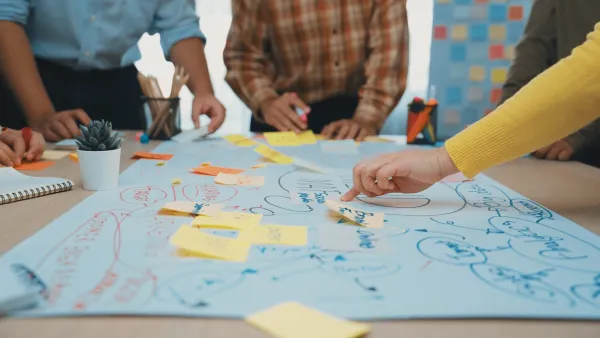 Close-up on group of people using large paper on a table and sticky notes to brainstorm.