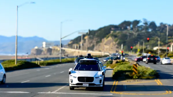 White Waymo Jaguar self-driving car with sensors on street next to ocean in California.