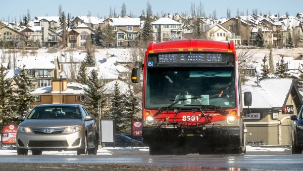 Red transit bus next to silver car on wet street.