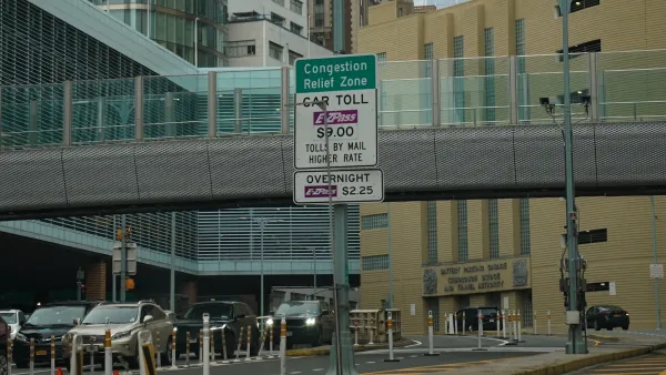 Sign for congestion pricing in front of an elevated pedestrian walkway with cars lined up underneath in New York City.