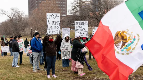 People holding up pro-immigrant signs at outdoor protest with Mexico flag in foreground.