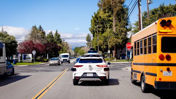 White Waymo self-driving car next to yellow school bus on street in Mountain View, California.