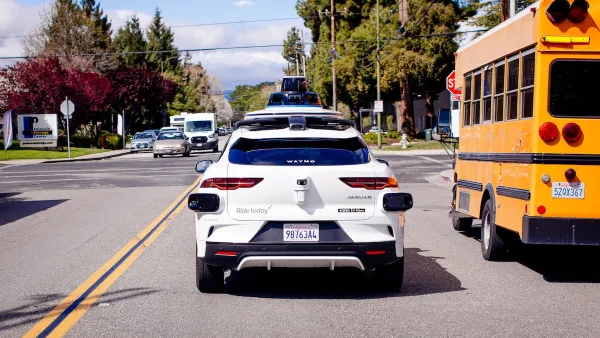White Waymo car driving next to yellow school bus.