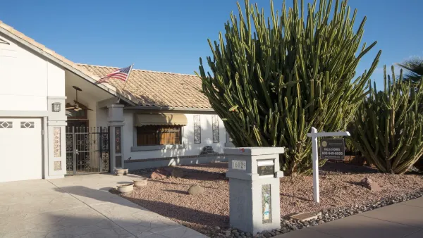 One-story beige home with large cactus in front yard with For Sale sign near sidewalk in Phoenix, Arizona.