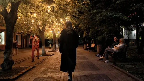 Woman in long coat walking on paved walkway lined with trees and benches at night.