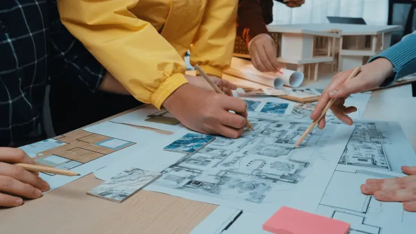 A group of students draw on a building plan printed on a large sheet of paper.