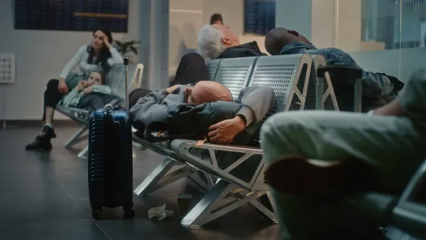 Man sleeping on airport seats in terminal with other people sitting around him.